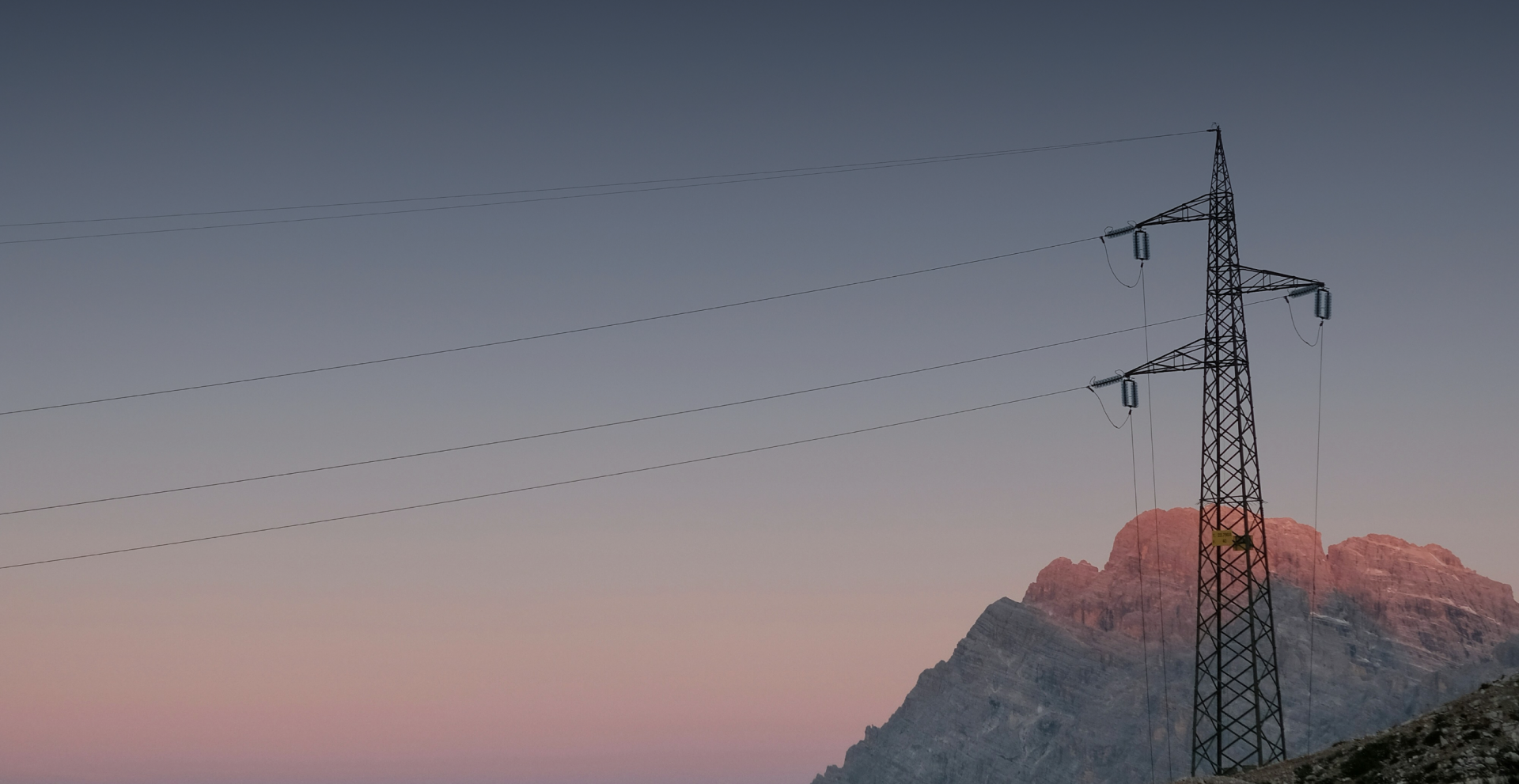 Imagen de fondo de una torre de alta tensión con una montaña de fondo en el atardecer.